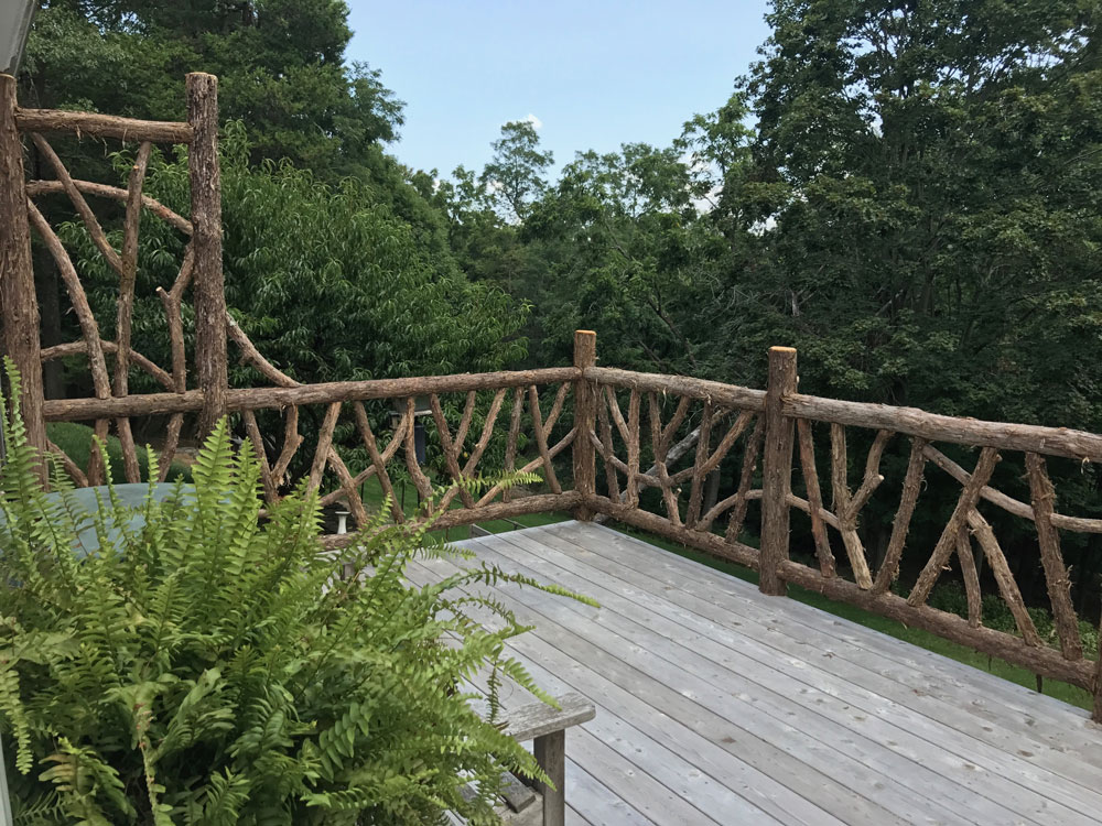 Rustic deck railings built using bark-on trees and branches titled the Burroughs Deck Railings